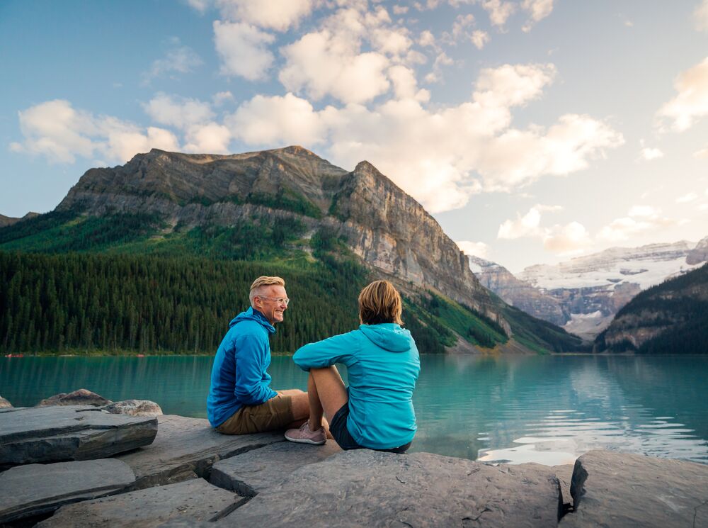 A couple sits on the lakeshore of Lake Louise at sunrise