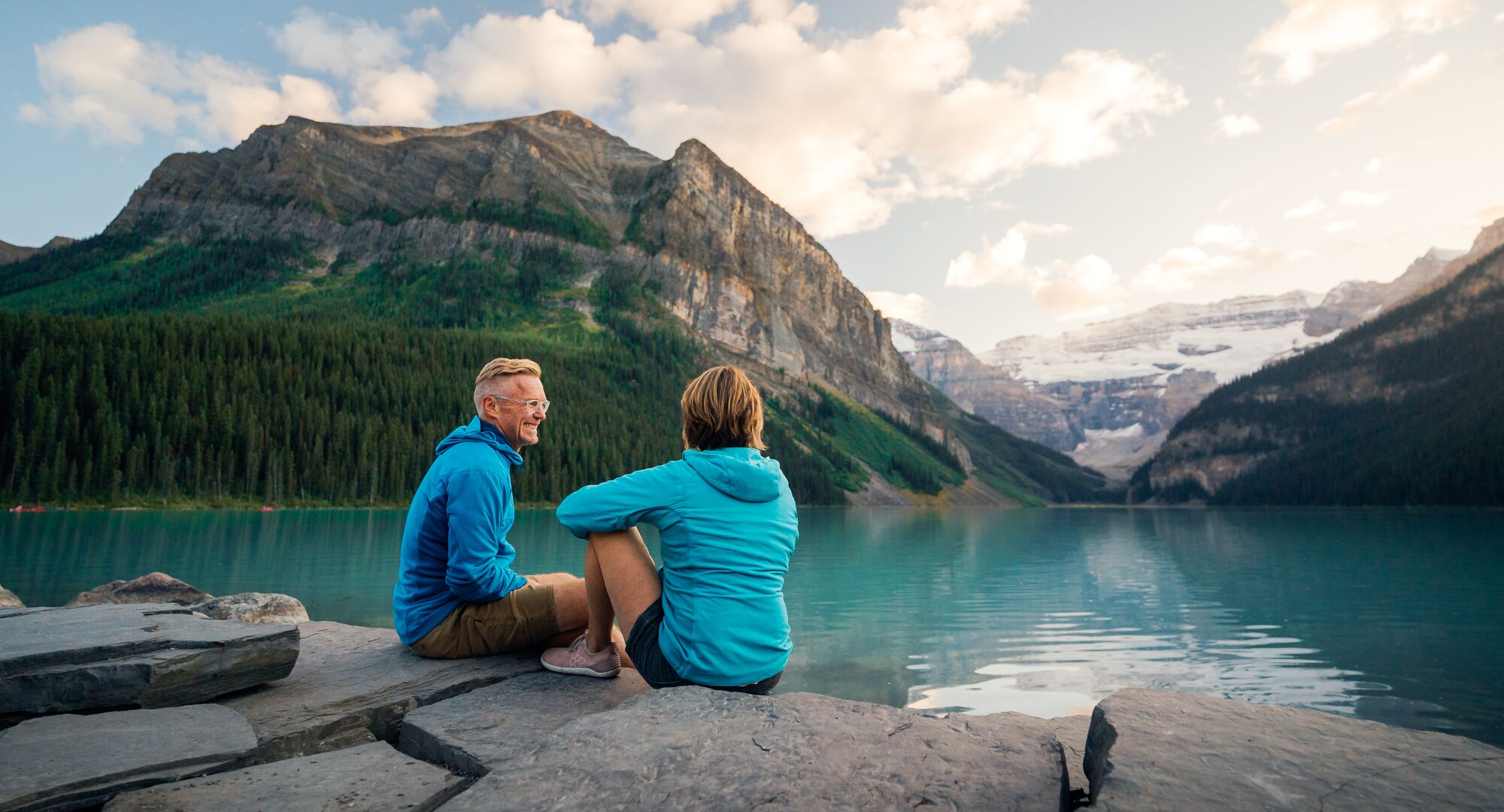 A couple sits on the lakeshore of Lake Louise at sunrise