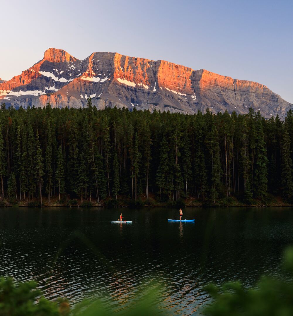 Two paddleboarders glide across Johnson Lake at Sunset with Mount Rundle lit up behind them, doing one of the most popular things to do in Banff in August.