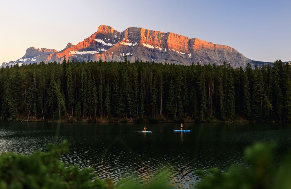 Two paddleboarders glide across Johnson Lake at Sunset with Mount Rundle lit up behind them, doing one of the most popular things to do in Banff in August.