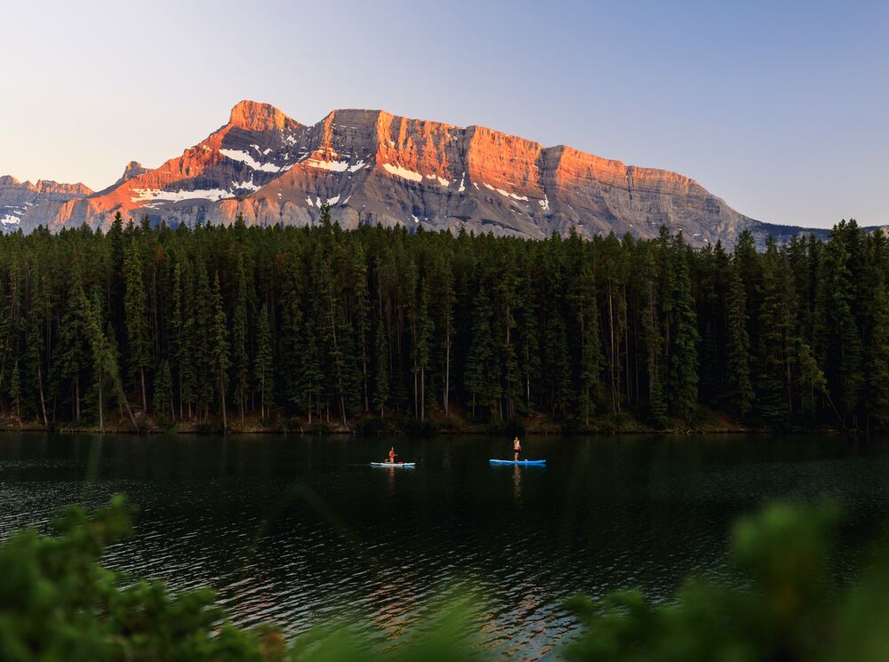 Two paddleboarders on Johnson Lake at sunset in Banff National Park.