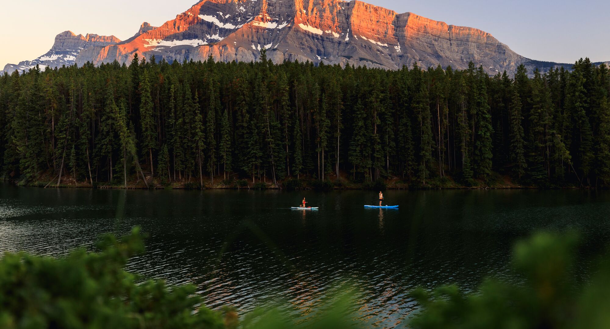 Two paddleboarders glide across Johnson Lake at Sunset with Mount Rundle lit up behind them, doing one of the most popular things to do in Banff in August.