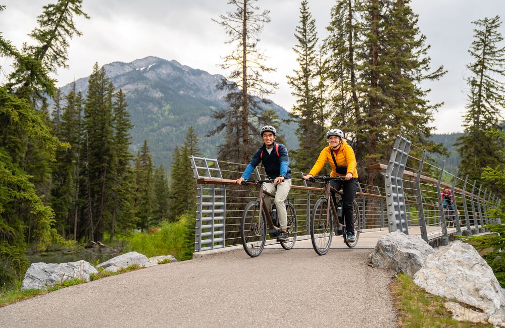 Two people e-biking on the pavement on Norquay Road in Banff