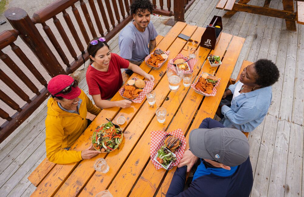 A group of friends enjoys food and drinks on a patio at Sunshine ski resort in Banff National Park. 