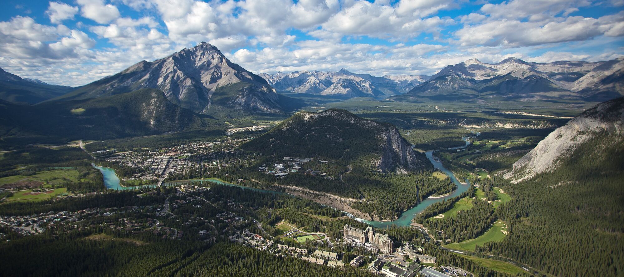 An aerial view of the town of Banff on a cloudy summer day showcasing Tunnel Mountain and Cascade