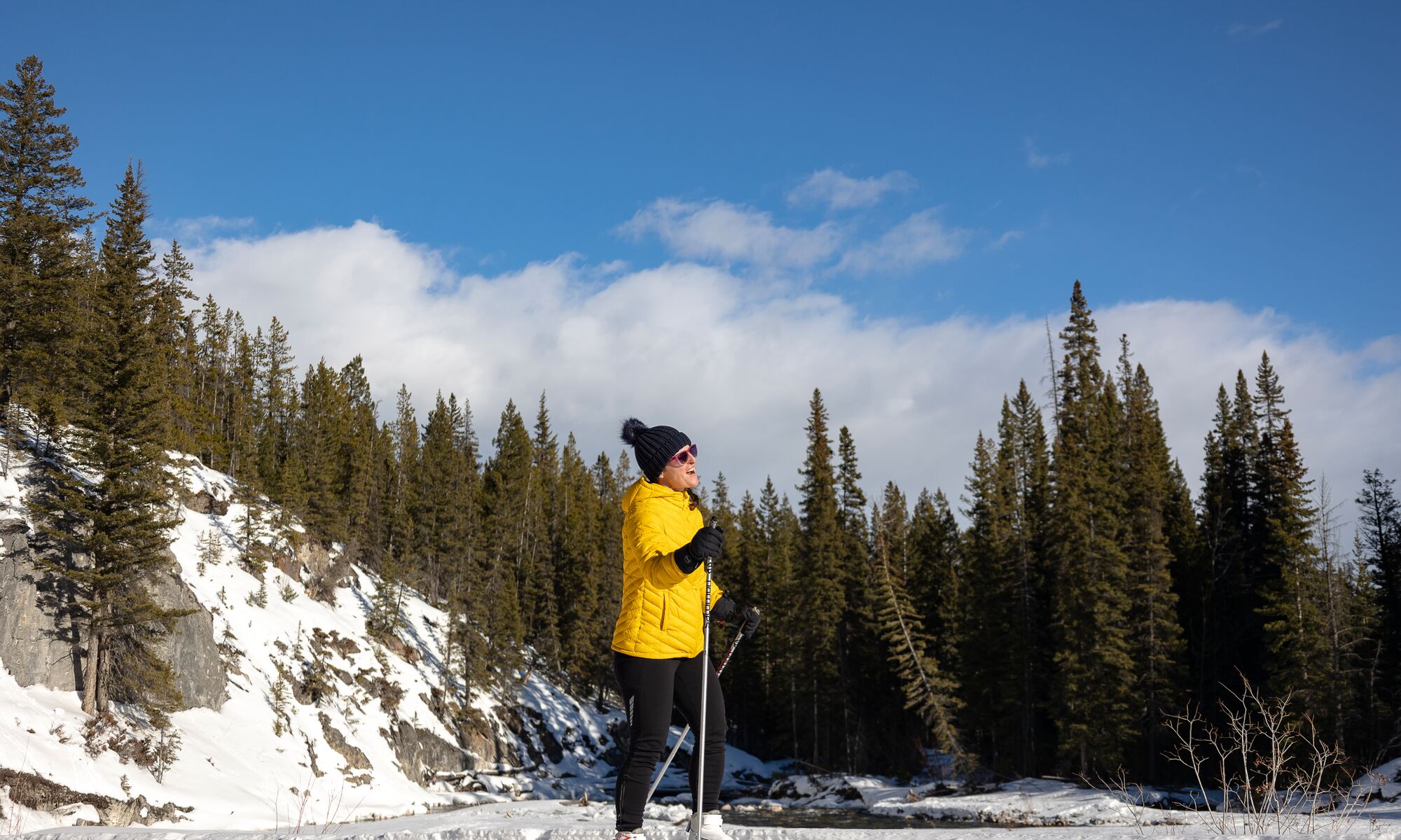 A woman in a yellow coat cross-country skis in Banff National Park.