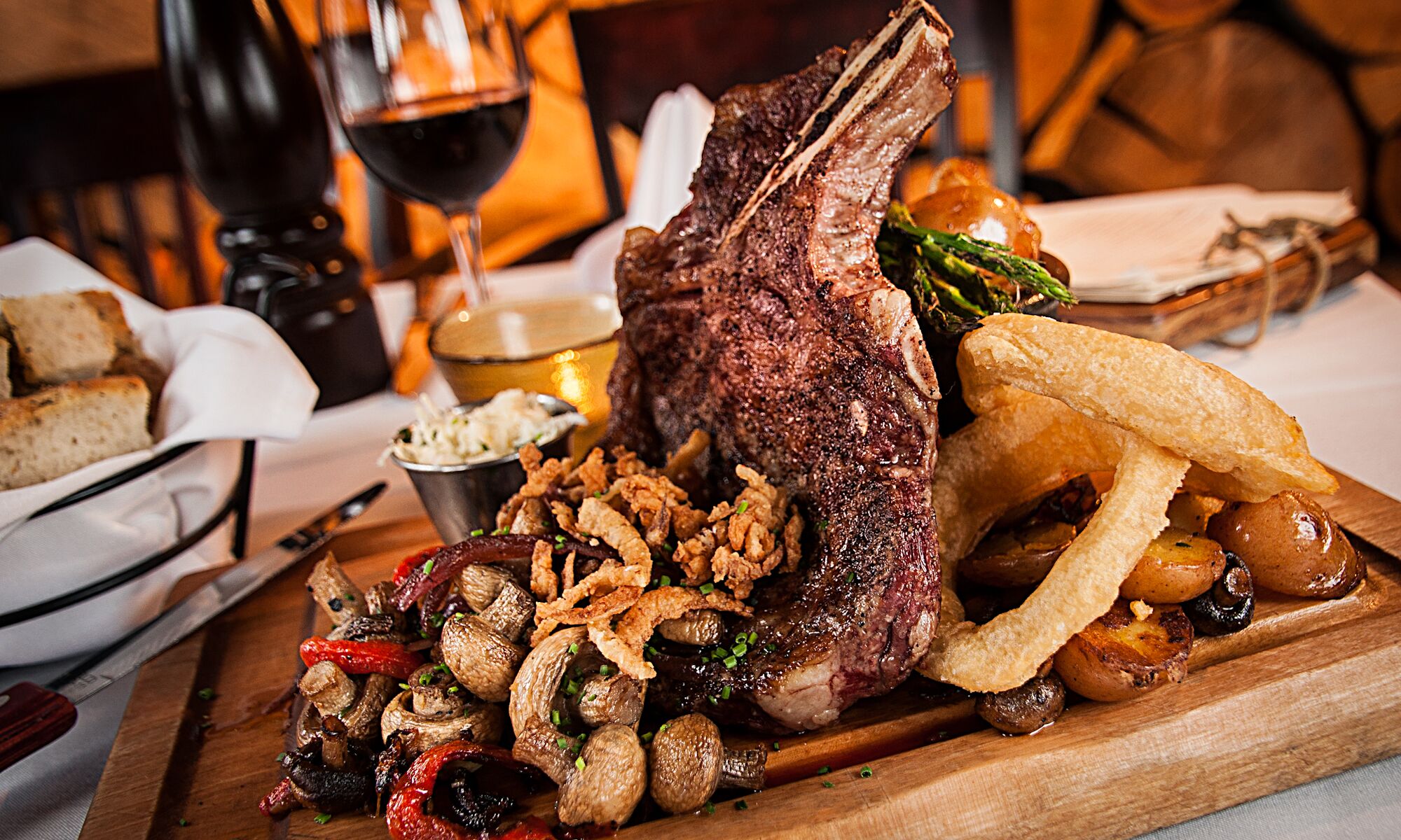 A roast lamb on a cutting board with veggies around it and a fire behind it at the Maple Leaf in Banff National Park.