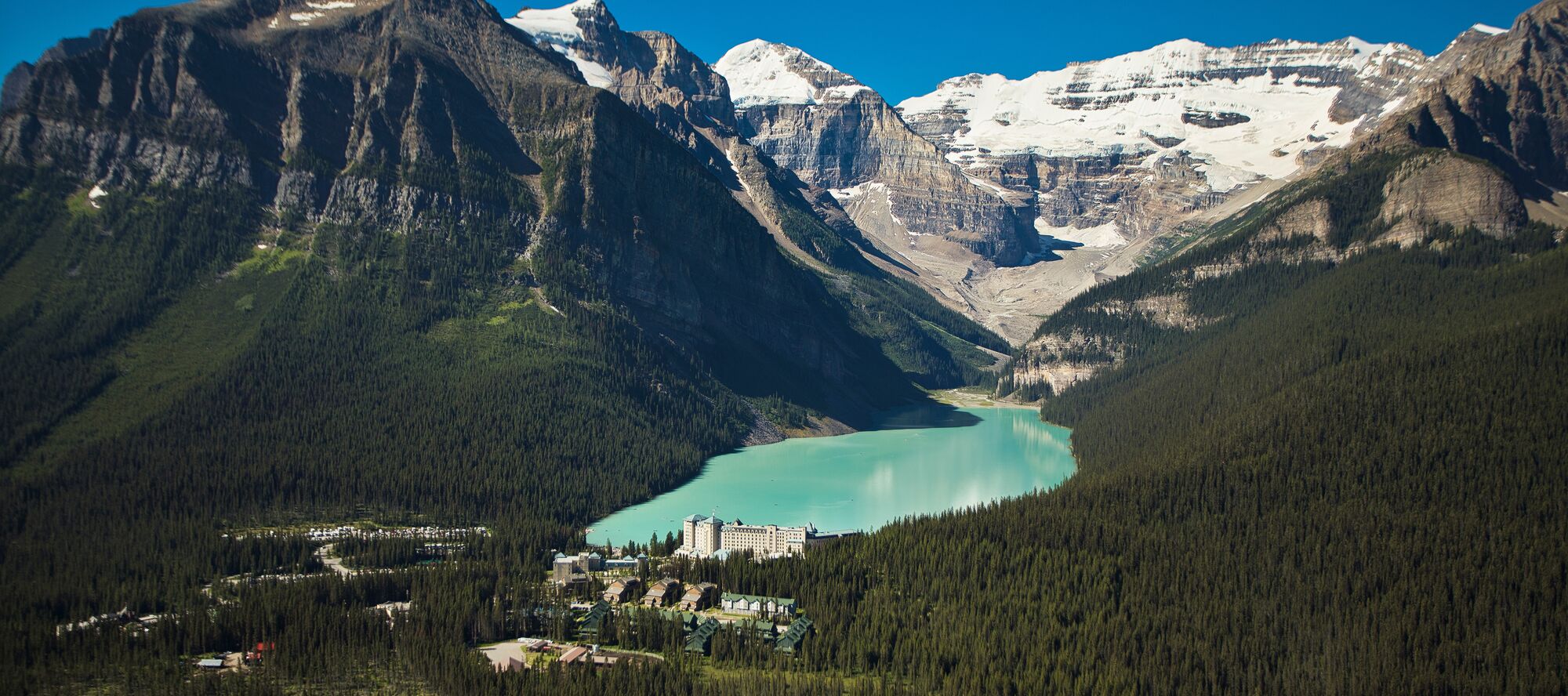 An aerial view of Fairmont Chateau Lake Louise in the summer with the turquoise lake and mountains in the background