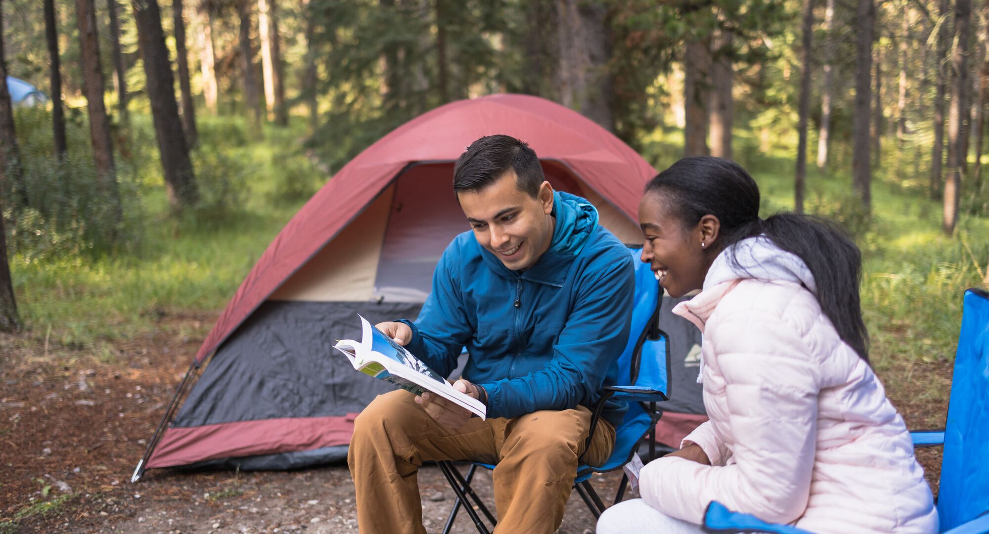 Two people reading a guidebook in front of their tent in a campground in Banff National Park.
