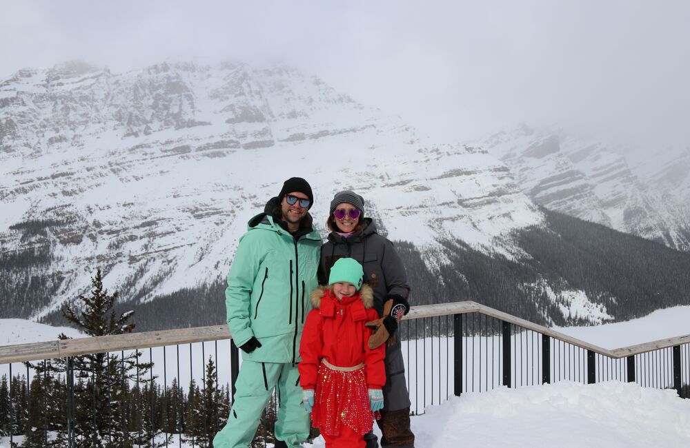 A family of three standing in front of mountain views at Lake Louise Ski Resort.