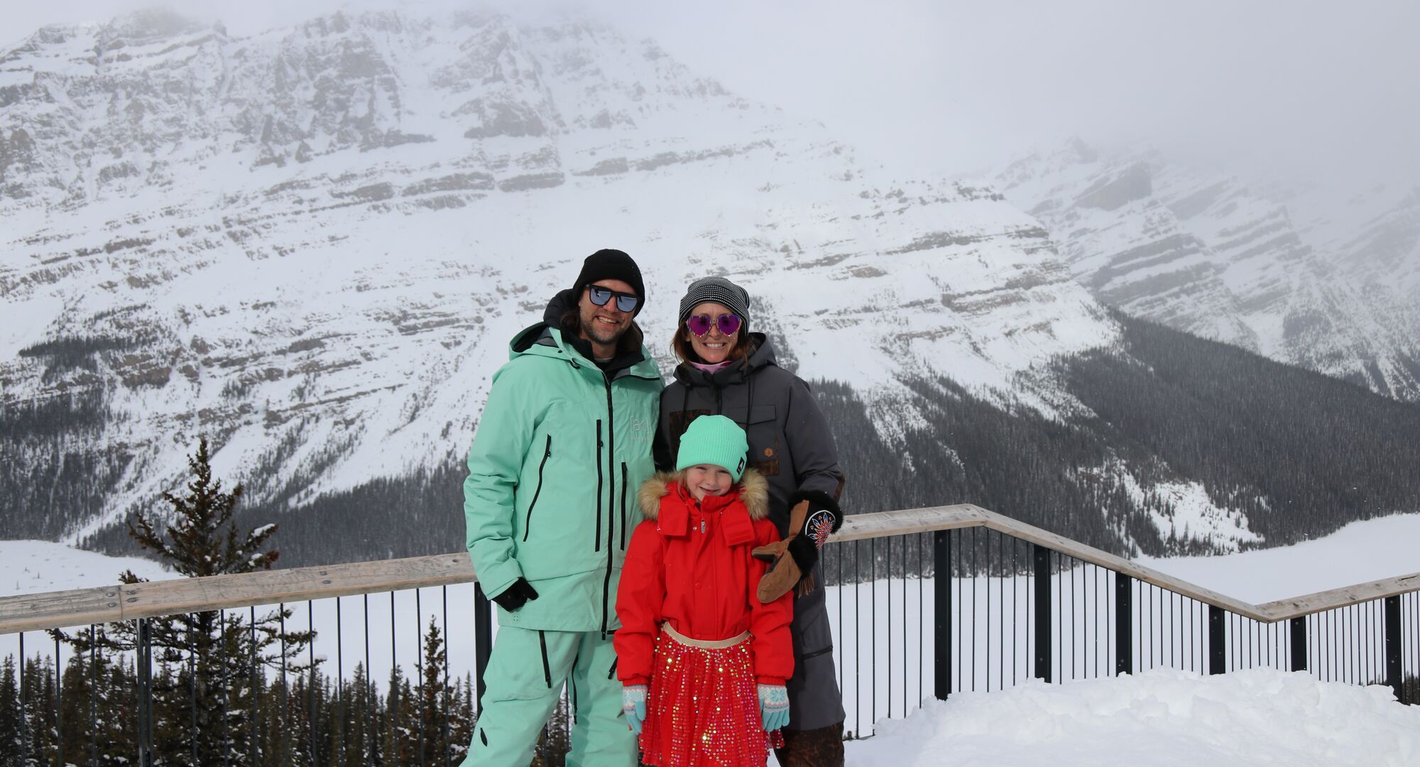 A family of three standing in front of mountain views at Lake Louise Ski Resort.