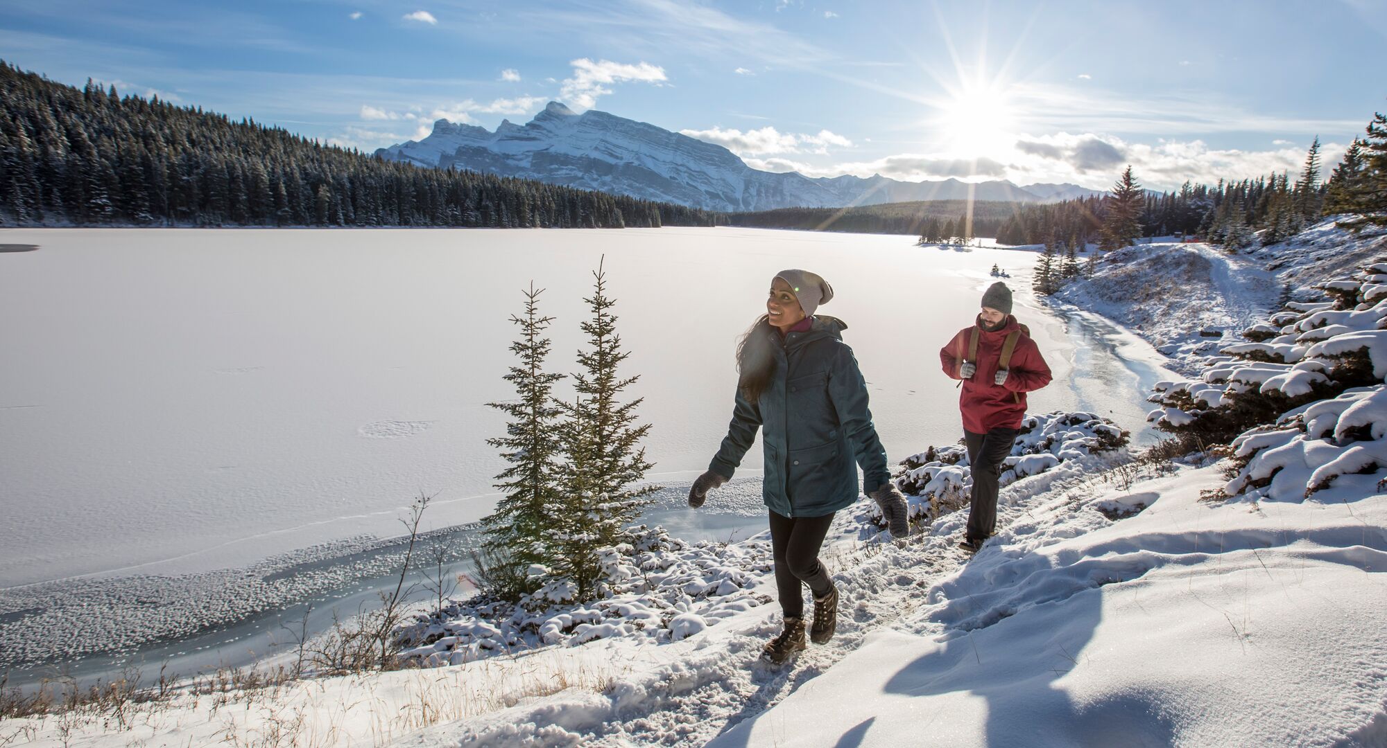 Two people hiking on the frozen lakeshore of Two Jack Lake in the winter