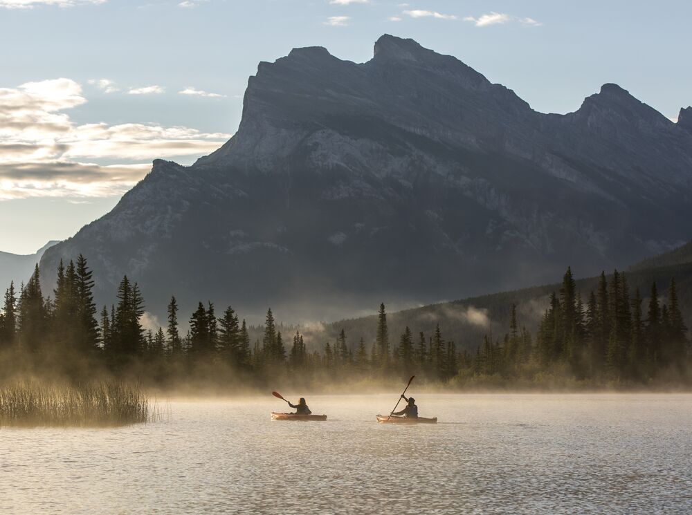 Two kayaks paddle on Vermilion Lakes at sunrise in Banff, Canada