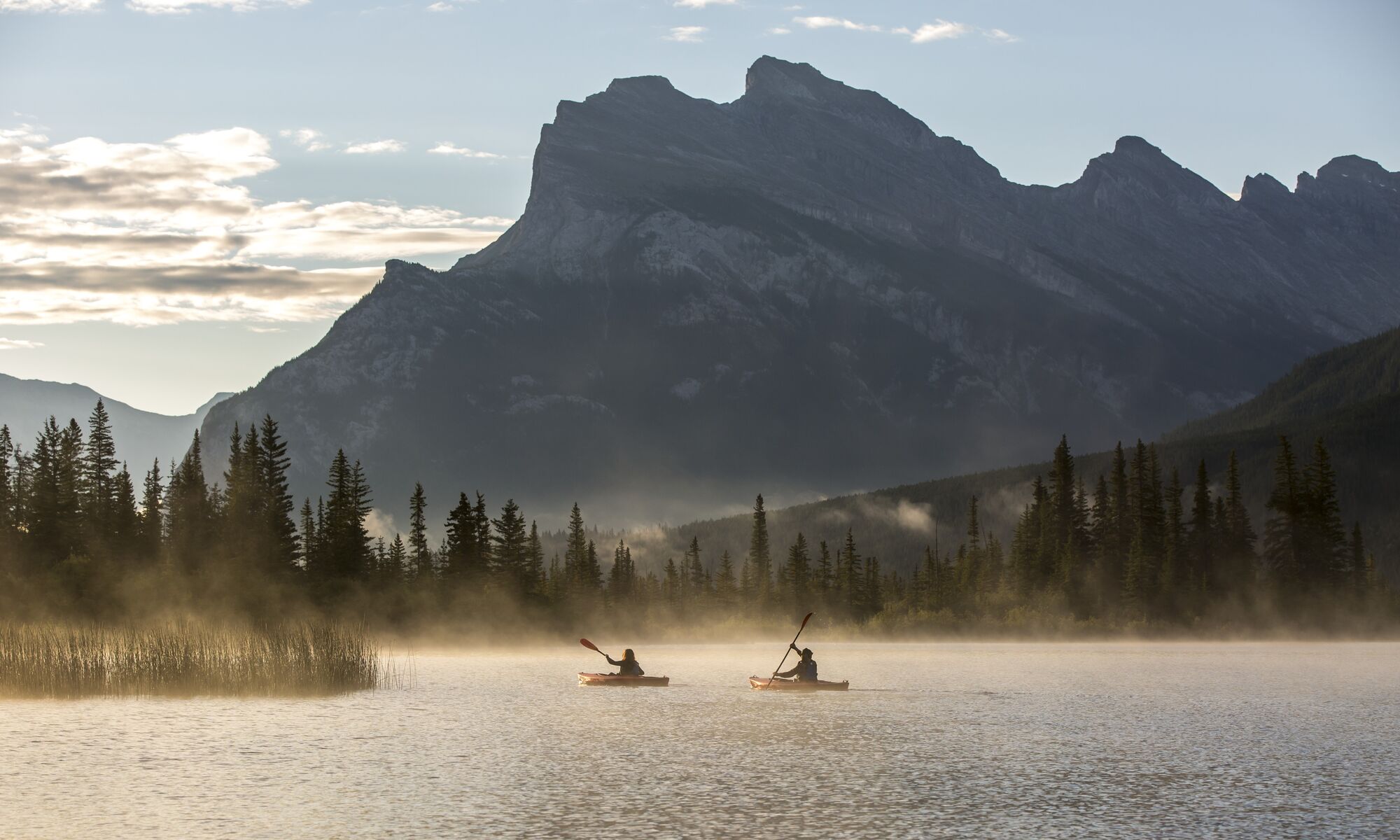 Two kayaks paddle on Vermilion Lakes at sunrise in Banff, Canada