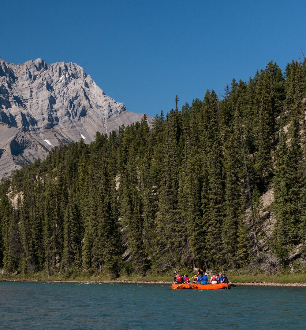 A raft floating down the Bow River with Cascade Mountain in the background