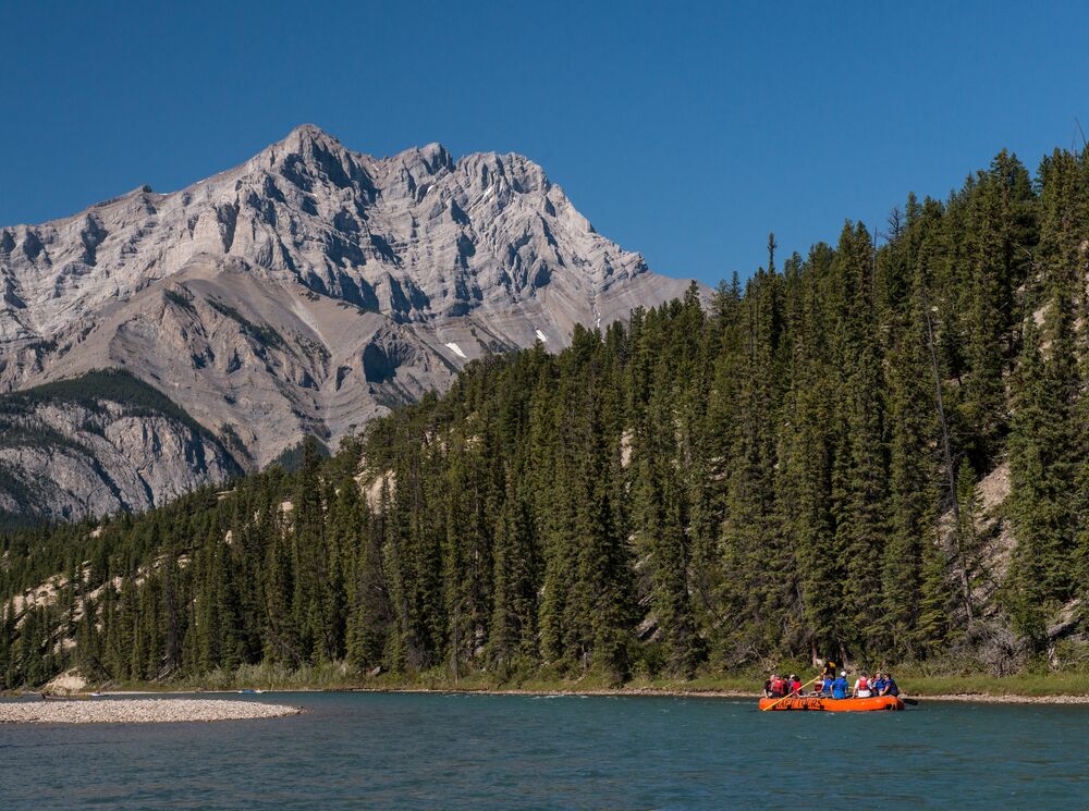 A raft floats on the Bow River in Banff National Park with Cascade Mountain in the background.