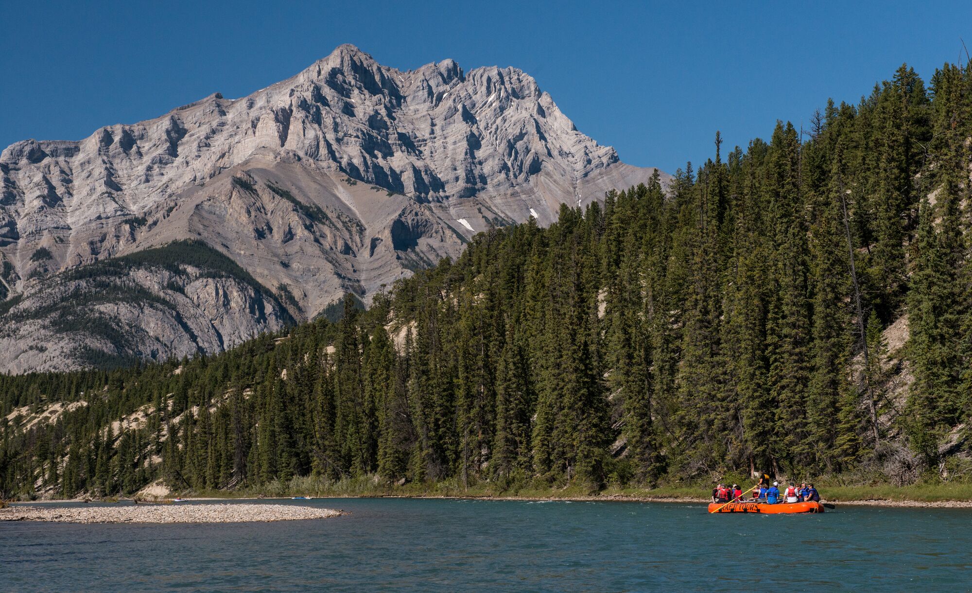 A raft floats on the Bow River in Banff National Park with Cascade Mountain in the background.