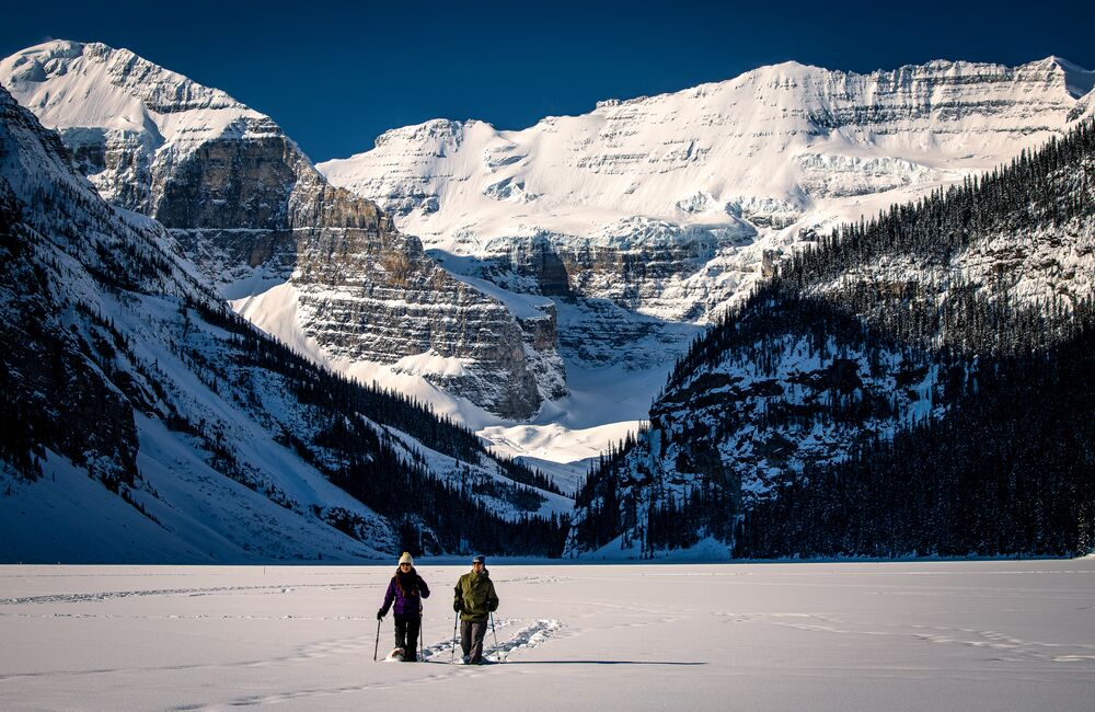 Two people walk on snowshoes on Lake Louise in Banff National Park.
