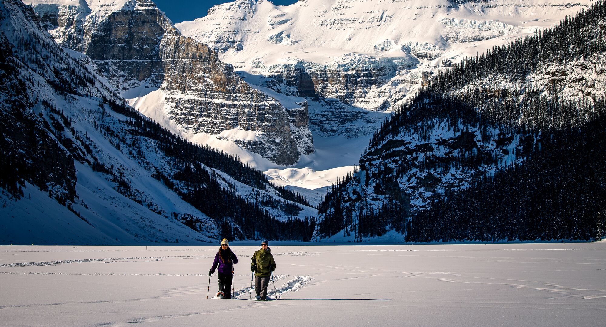Two people walk on snowshoes on Lake Louise in Banff National Park.