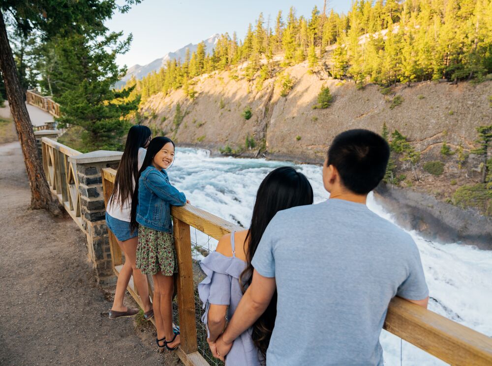 A family looks out over Bow Falls from the Bow River Pathway.