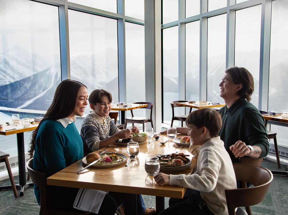 A family dines at Sky Bistro at the Banff Gondola with mountains out the window in Banff National Park.