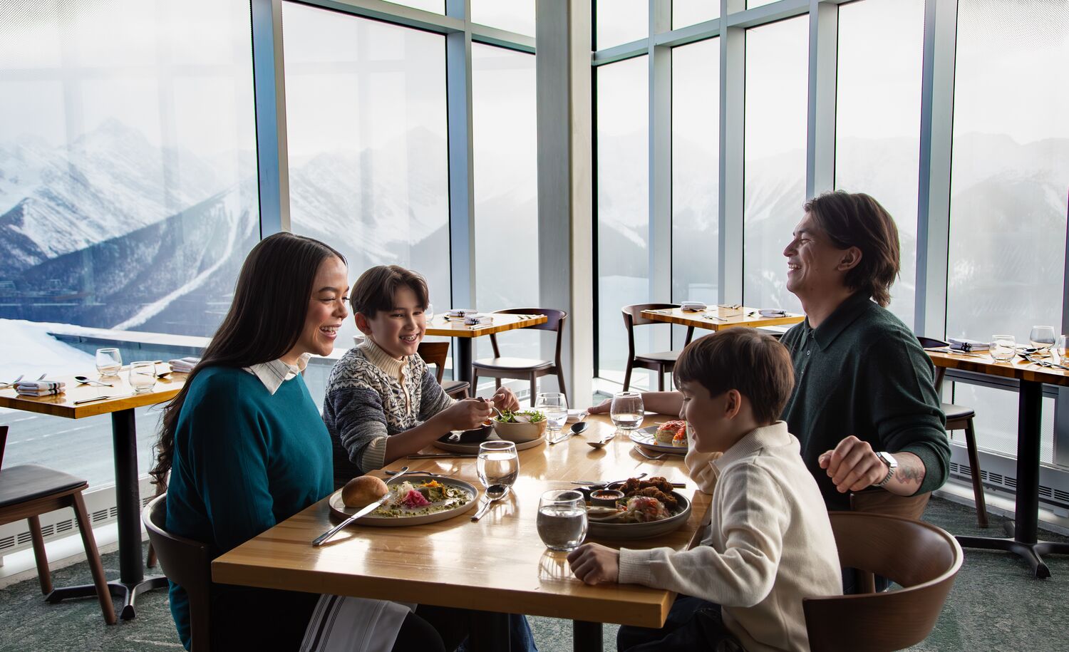 A family dines at Sky Bistro at the Banff Gondola with mountains out the window in Banff National Park.