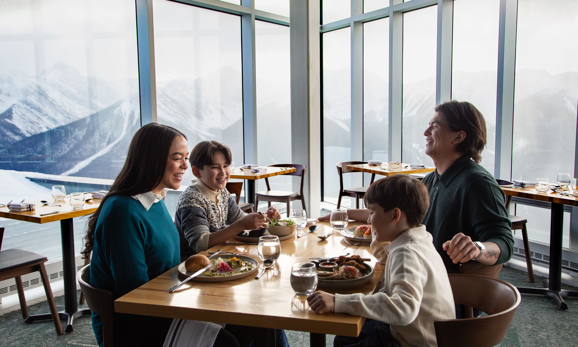 A family dines at Sky Bistro at the Banff Gondola with mountains out the window in Banff National Park.