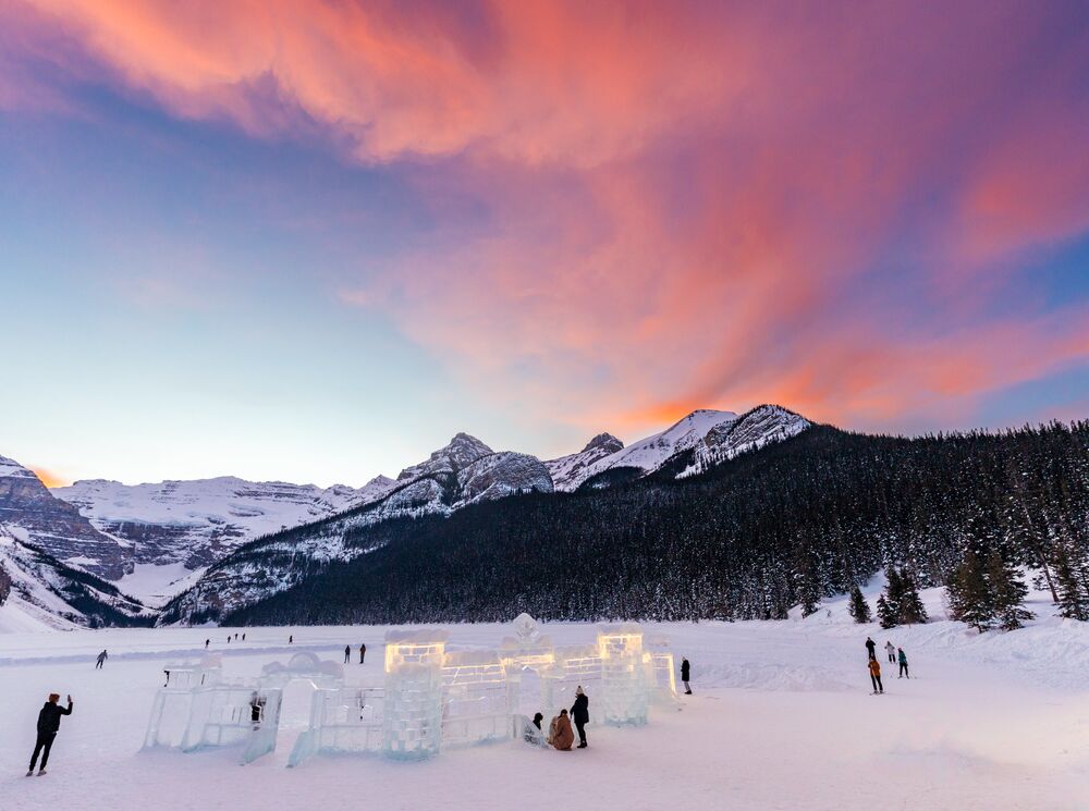 Lake Louise covered in snow with a ice castle in the foreground and orange clouds above mountains in Banff National Park.