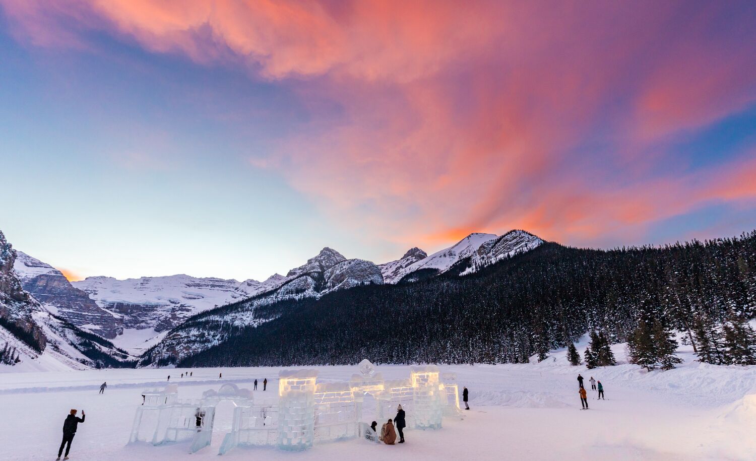 Lake Louise covered in snow with a ice castle in the foreground and orange clouds above mountains in Banff National Park.