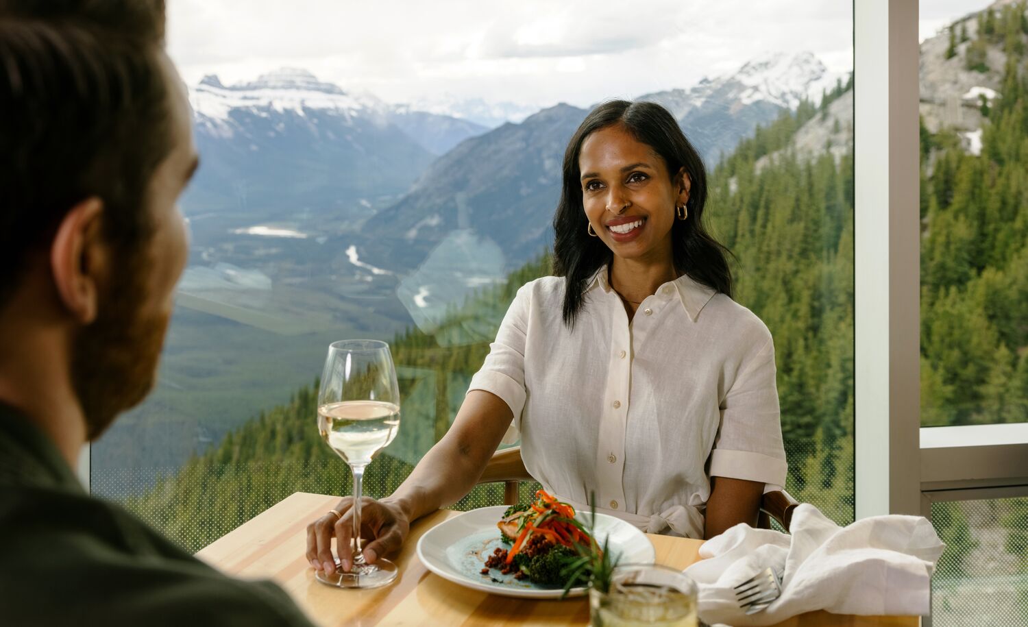 A couple enjoys a meal at the top of the Banff Gondola with views of surrounding mountain peaks in Banff National Park