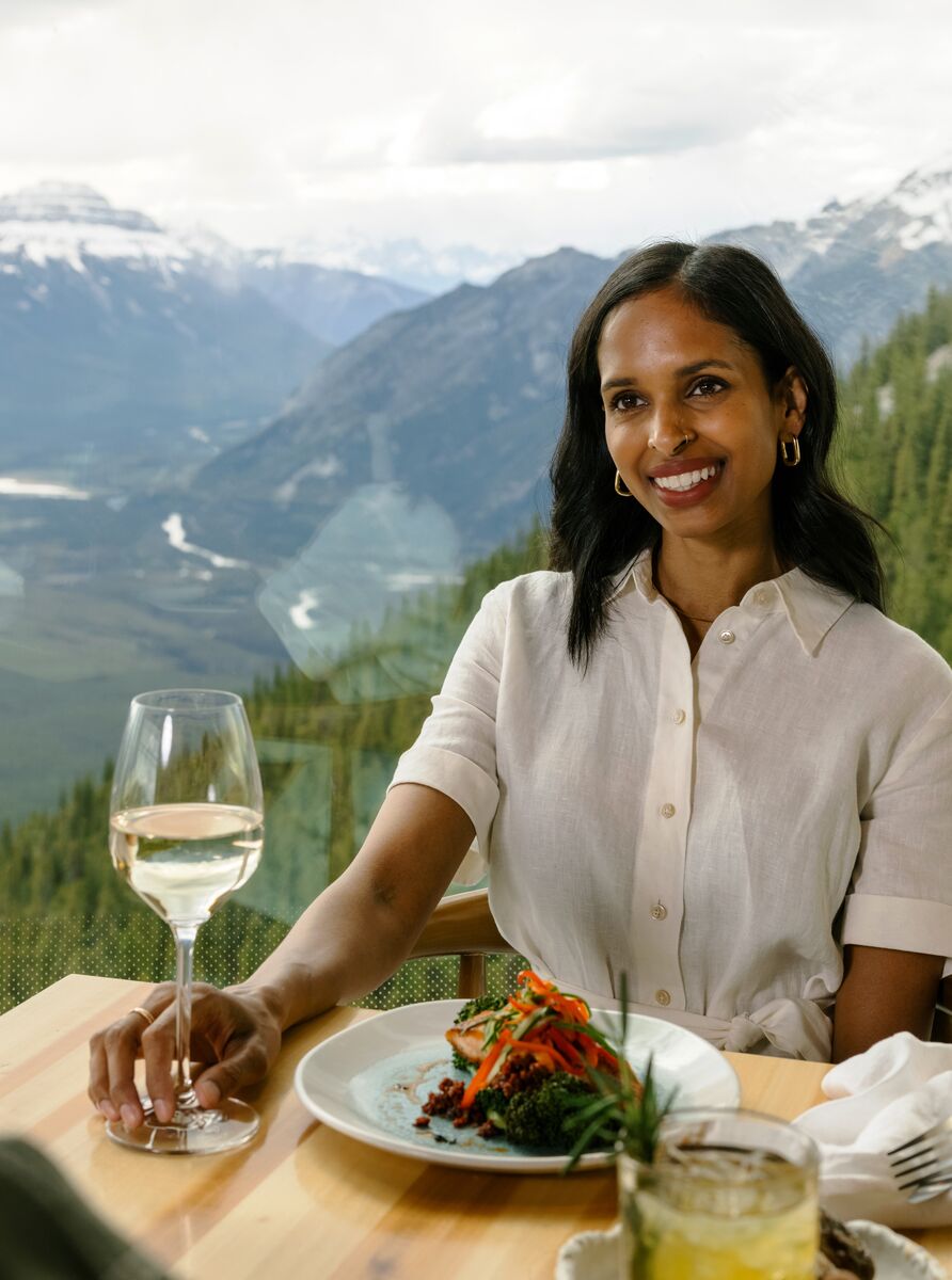 A couple enjoys a meal at the top of the Banff Gondola with views of surrounding mountain peaks in Banff National Park
