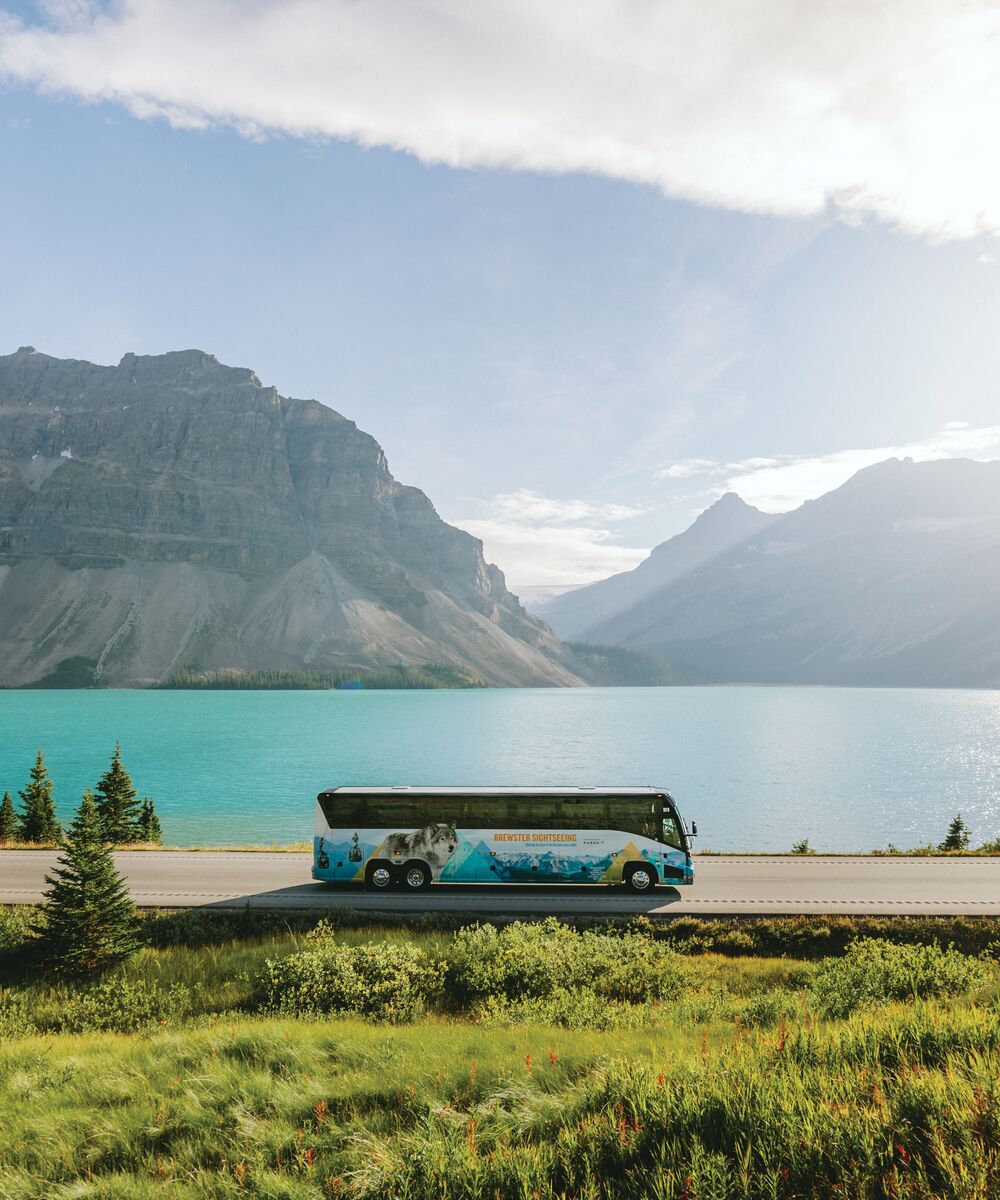 A tour bus driving the Icefields parkway with Bow Lake in the background.