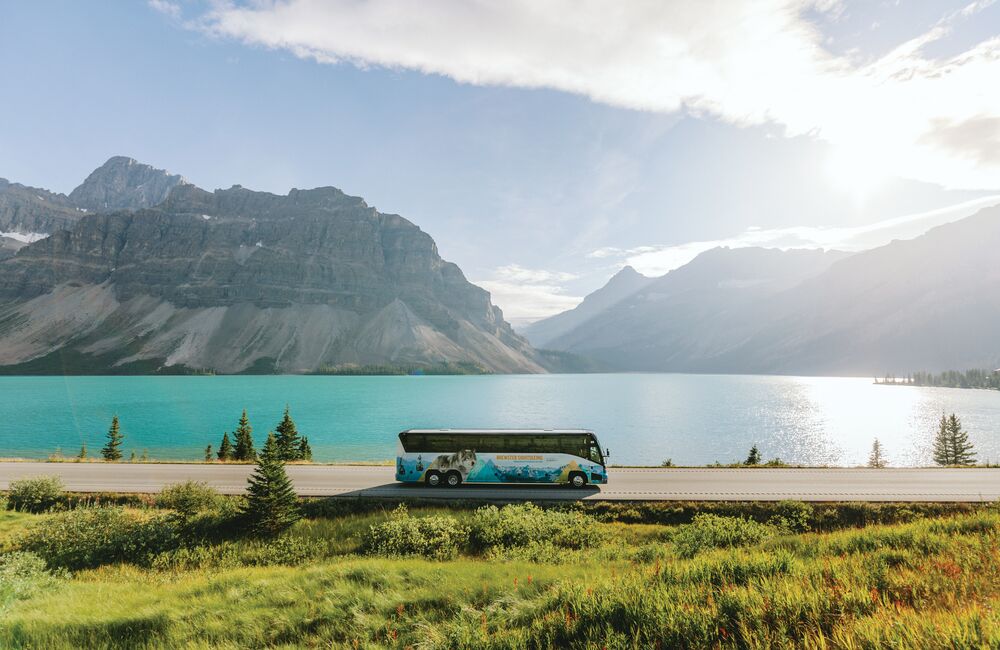 A sightseeing tour bus driving the Icefields Parkway with Bow Lake in the background