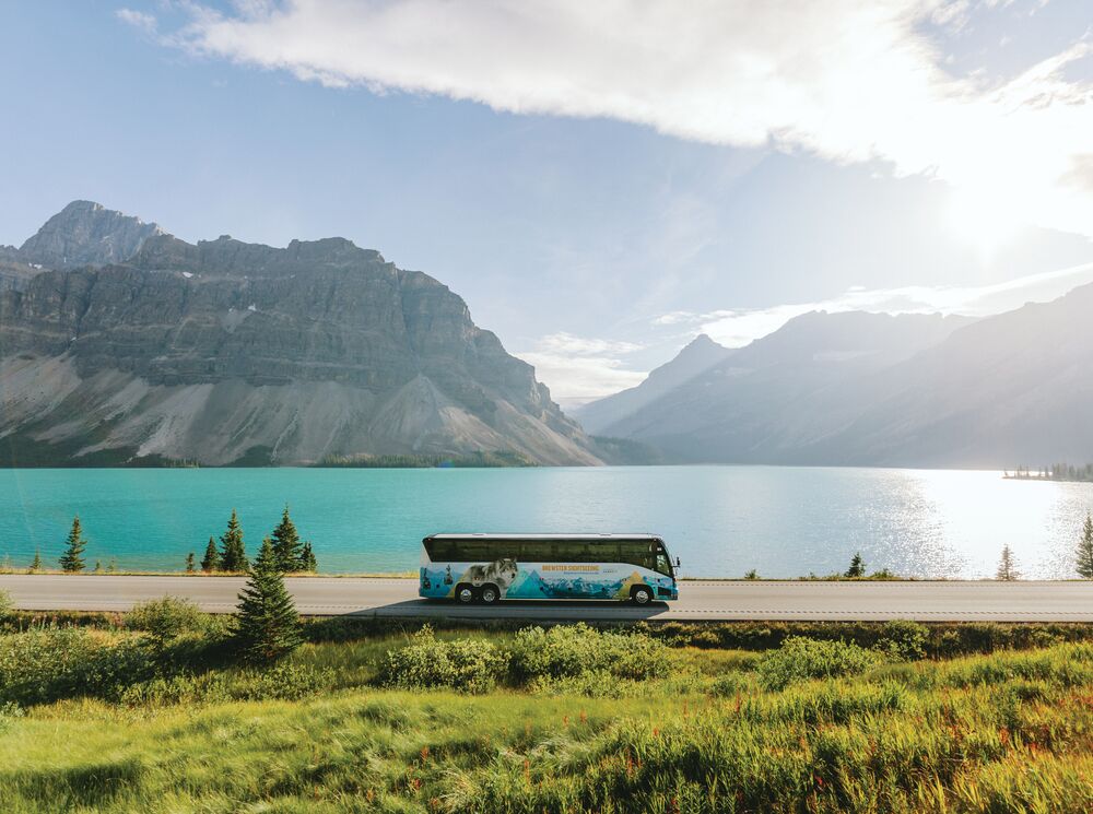 A sightseeing tour bus driving the Icefields Parkway with Bow Lake in the background