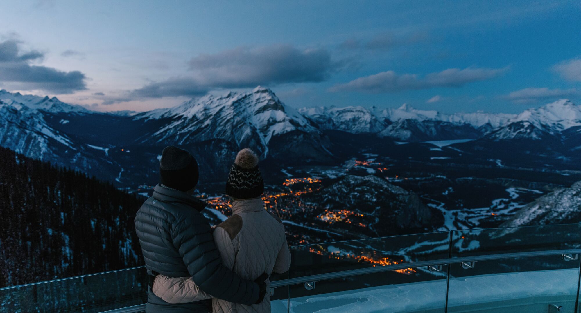 Two people taking in the views of the mountains from the viewing deck at the top of the Banff Gondola