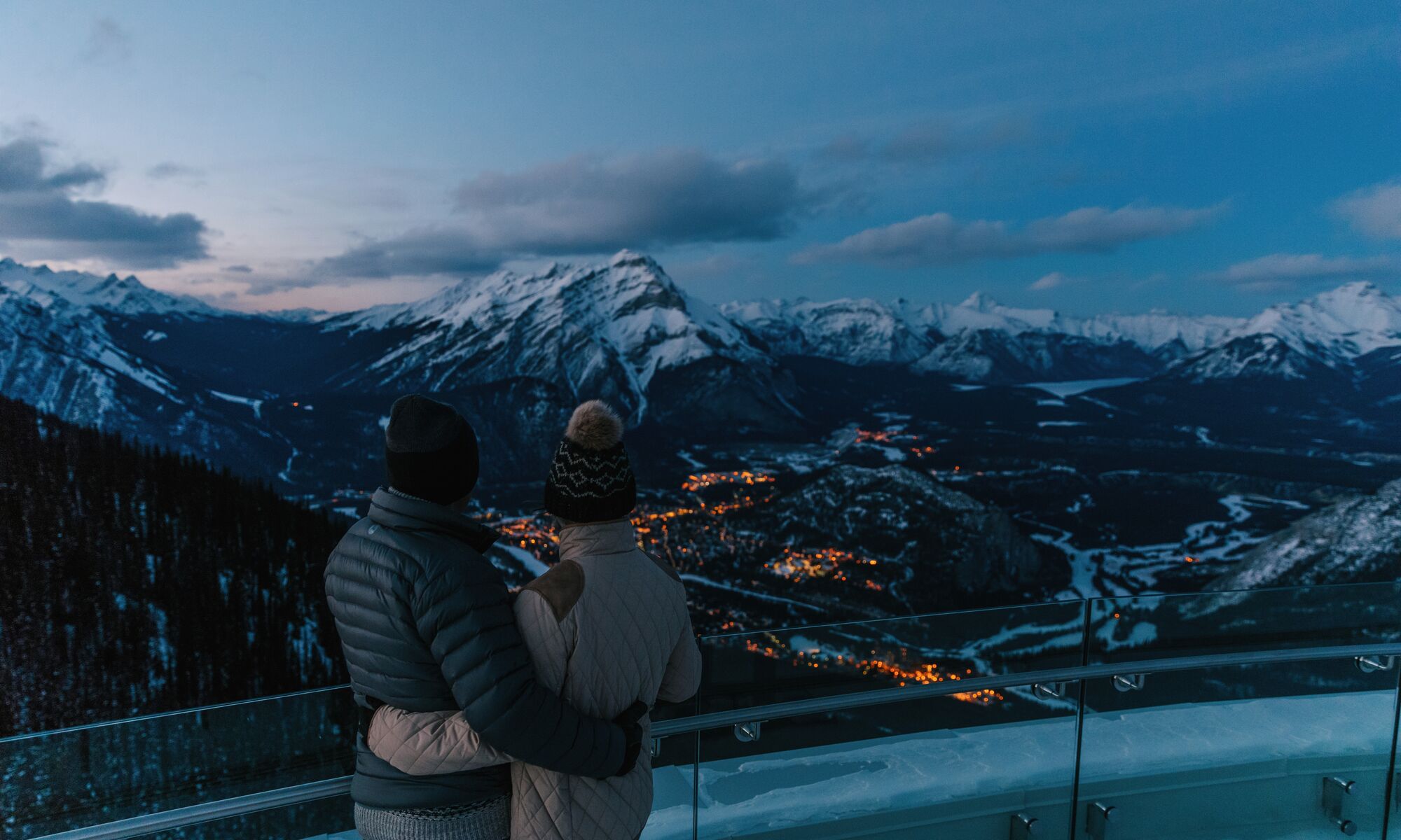 A couple looks out from the observation deck of the Banff Gondola towards Cascade Mountain and the town of Banff in Banff National Park.