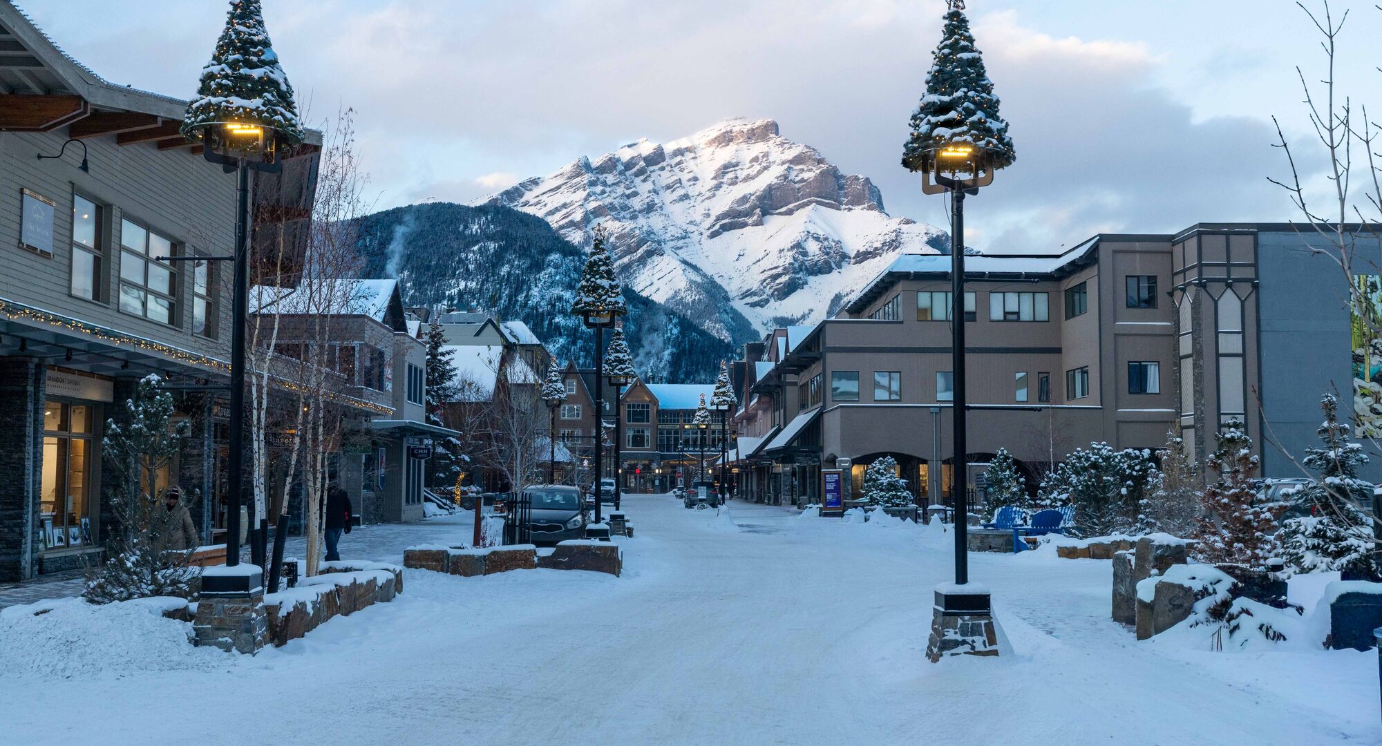 Bear Street in downtown Banff at dusk with Cascade Mountain in the background and snow covering the streets and mountains.