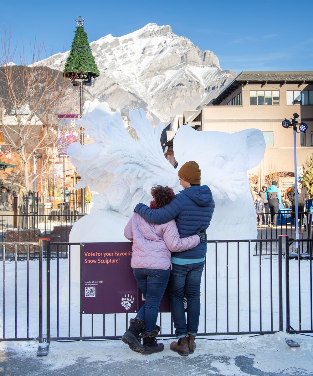 Two people standing in front of a giant snow sculpture during the SnowDays festival in Banff National Park