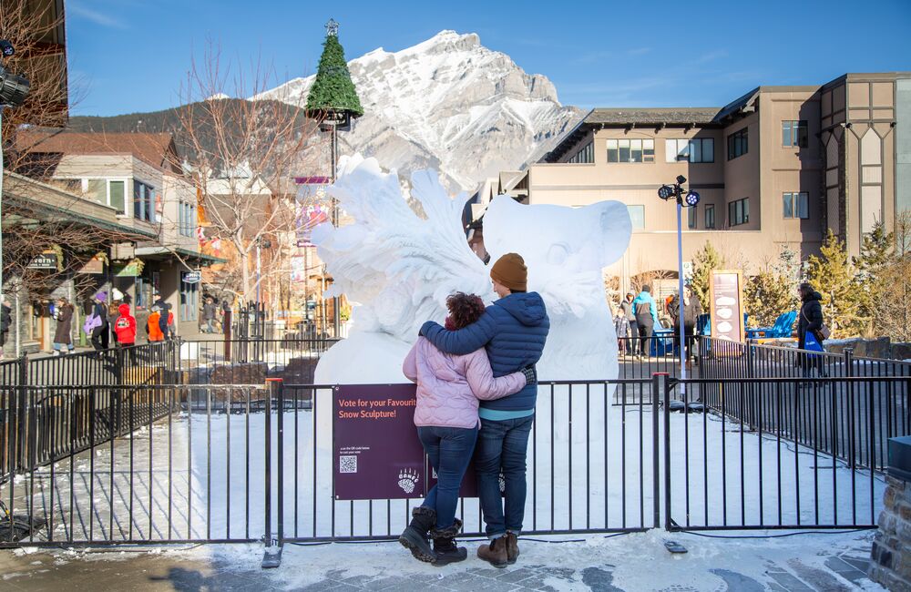 Two people standing in front of a giant snow sculpture during the SnowDays festival in Banff National Park