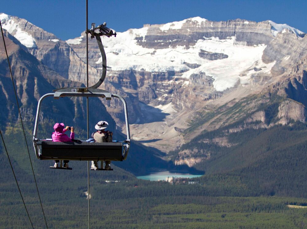 Two people ride the Lake Louise Summer Sightseeing Gondola looking out towards Lake Louise in Banff National Park.