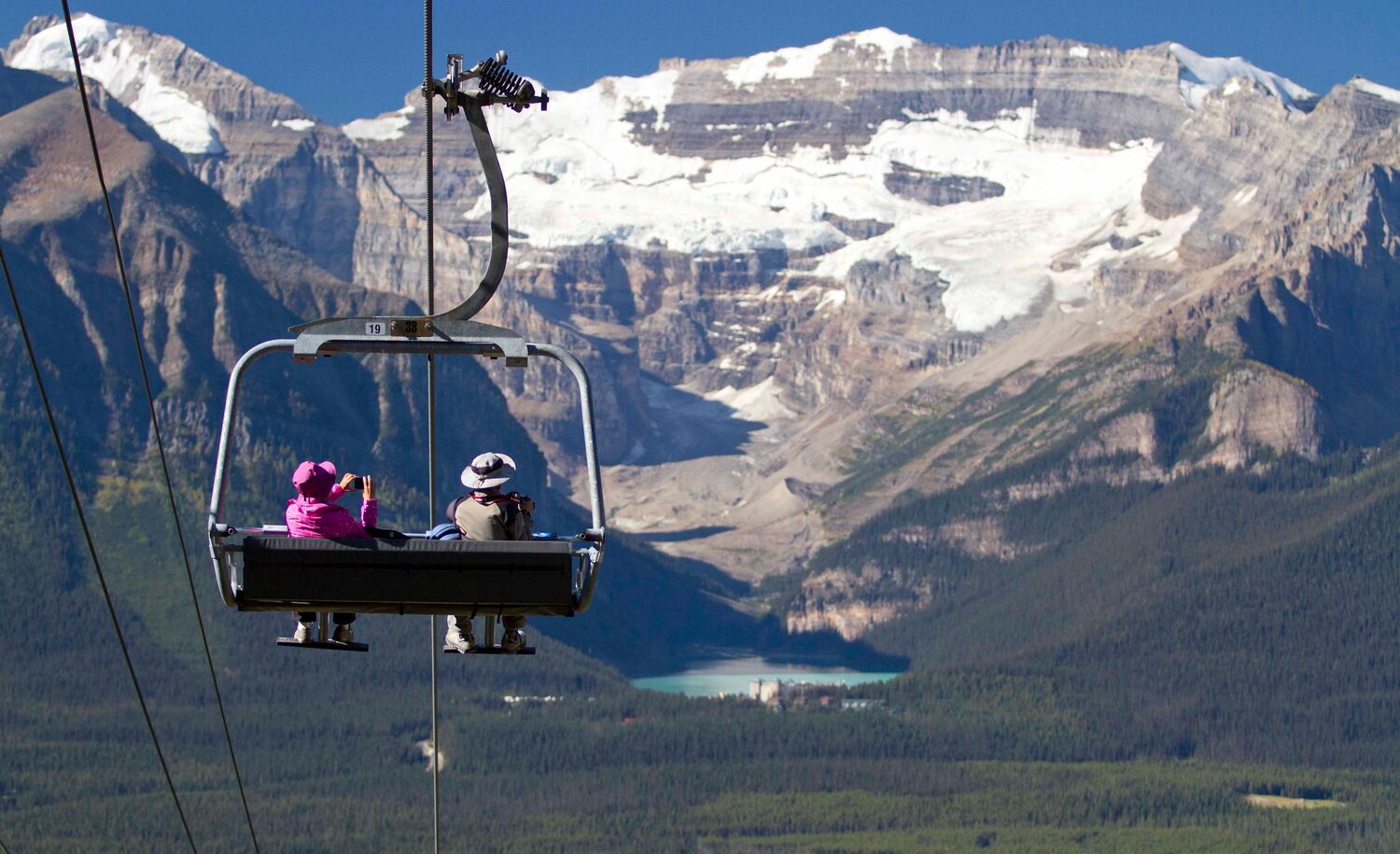 Two people ride the Lake Louise Summer Sightseeing Gondola looking out towards Lake Louise in Banff National Park.