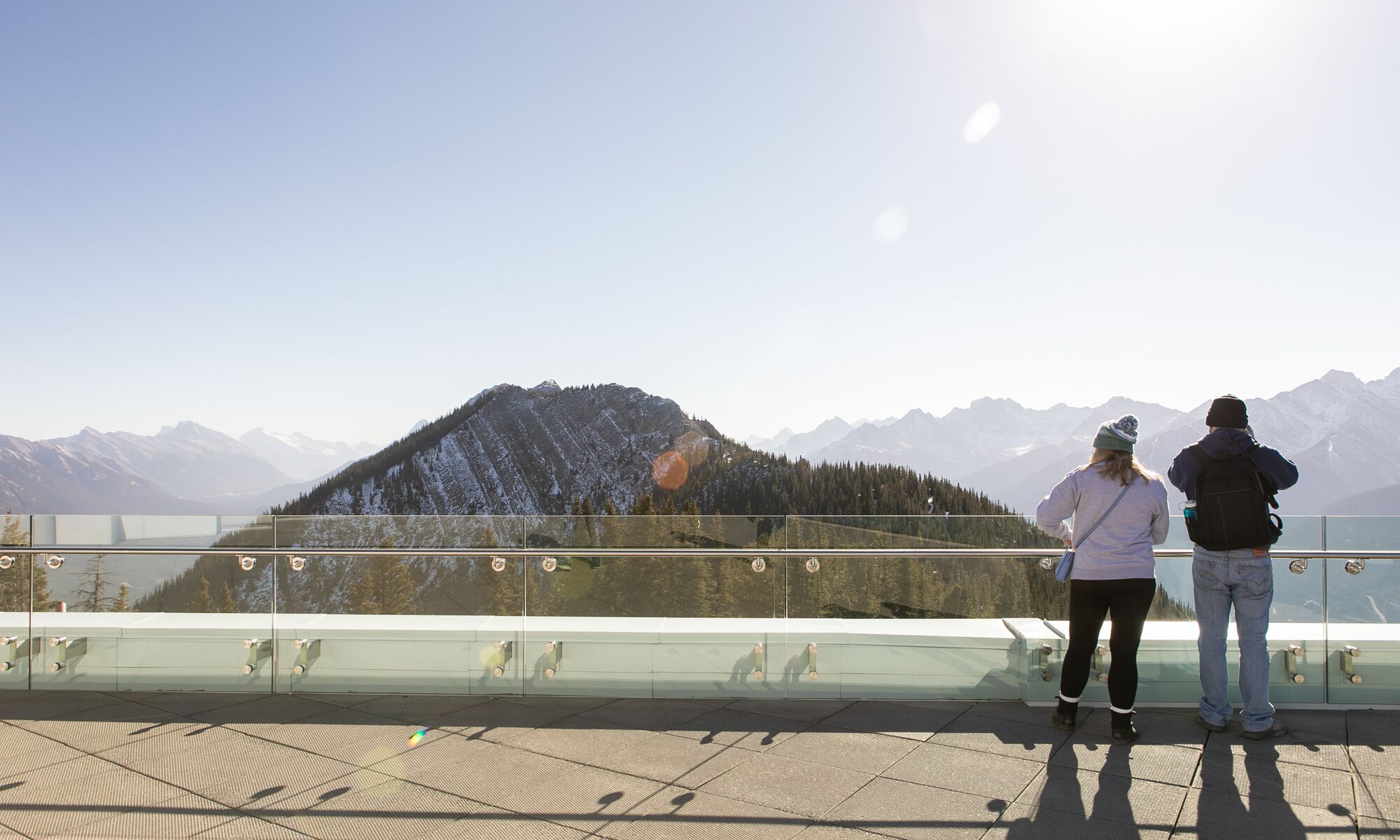 Two people look over the edge at the Banff Gondola with a mountain in the background.