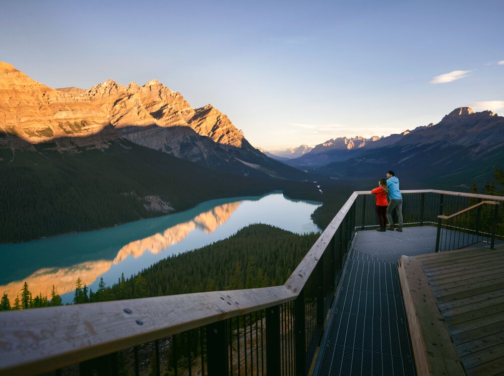 A couple stand on the viewing deck looking out at the view of Peyto Lake and the surrounding mountains.