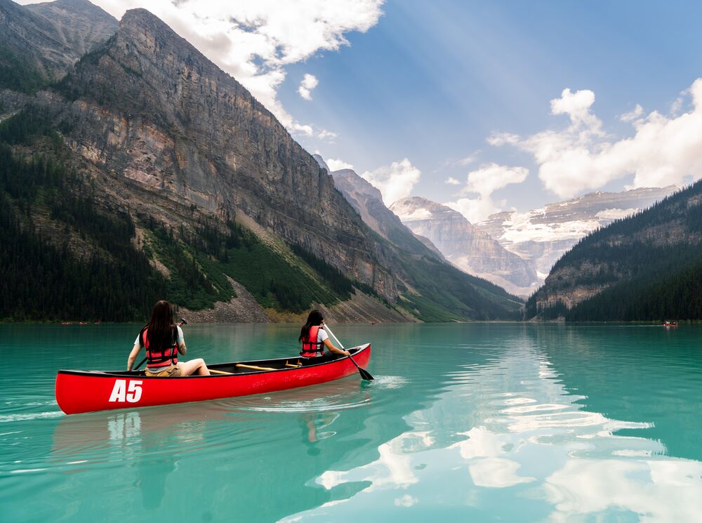 Two friends paddle in a canoe in an open lake surrounded by mountains in Lake Louise.