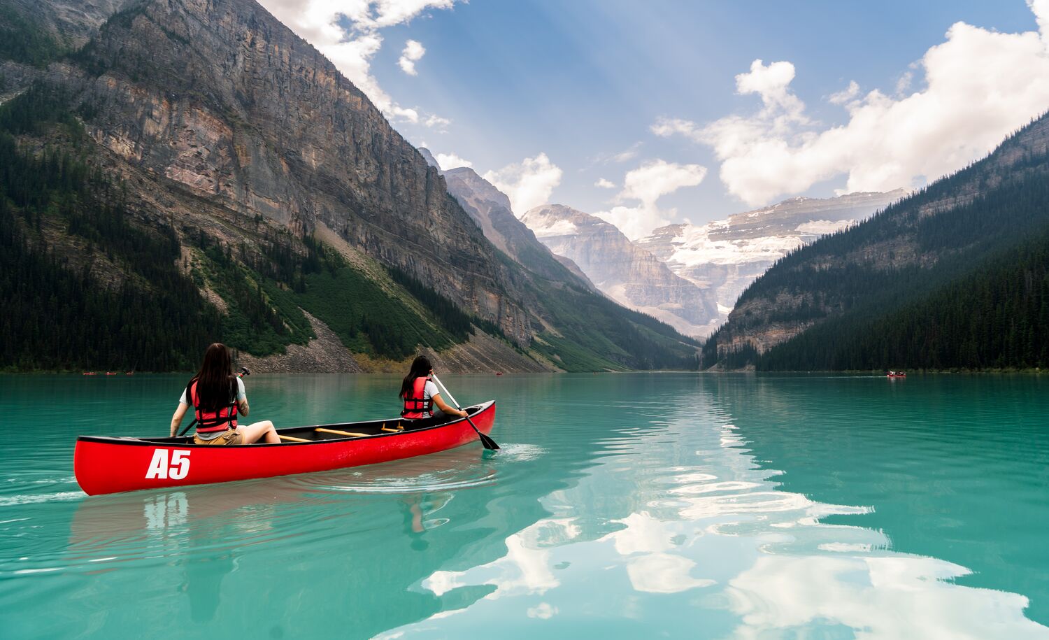 Two friends paddle in a canoe in an open lake surrounded by mountains in Lake Louise.