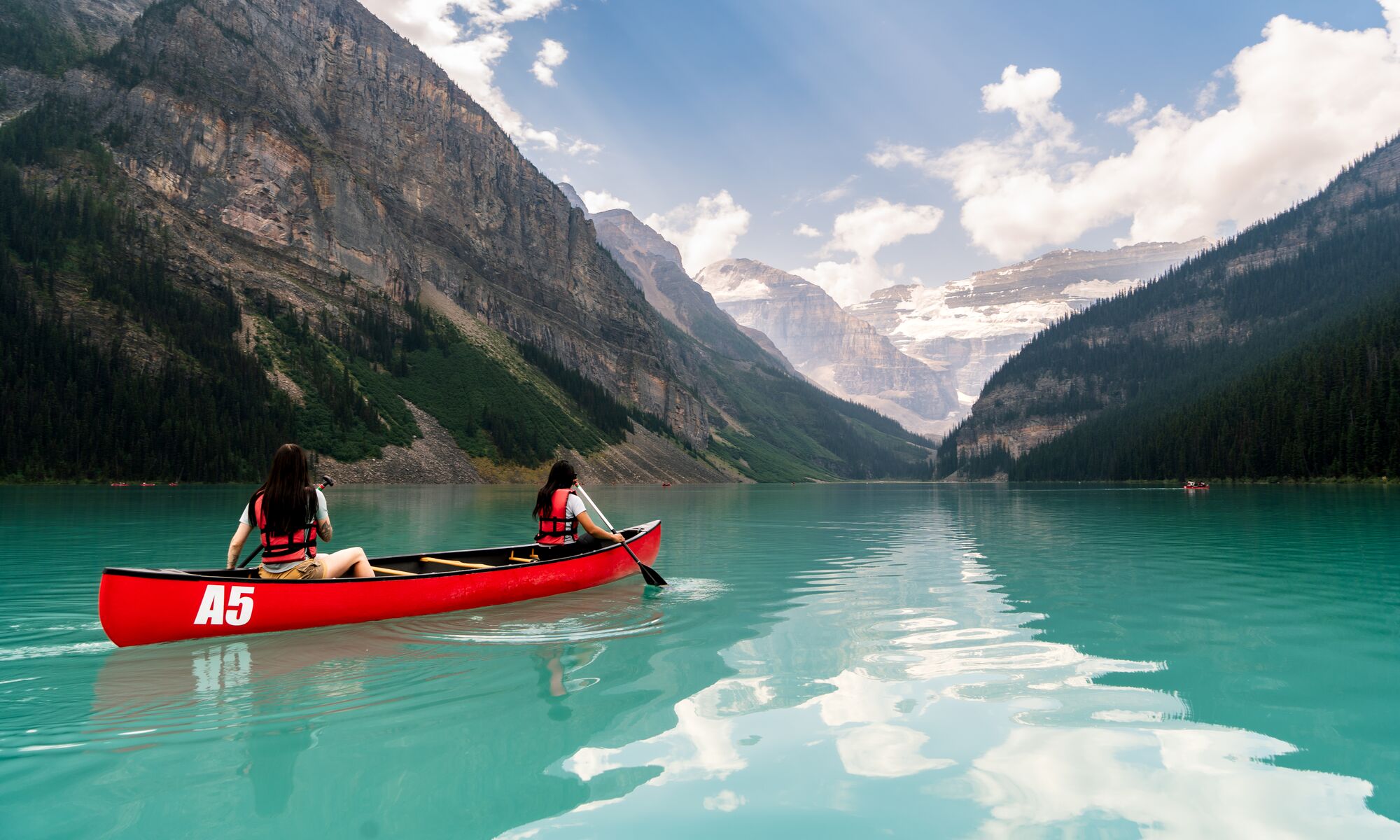 Two friends paddle in a canoe in an open lake surrounded by mountains in Lake Louise.