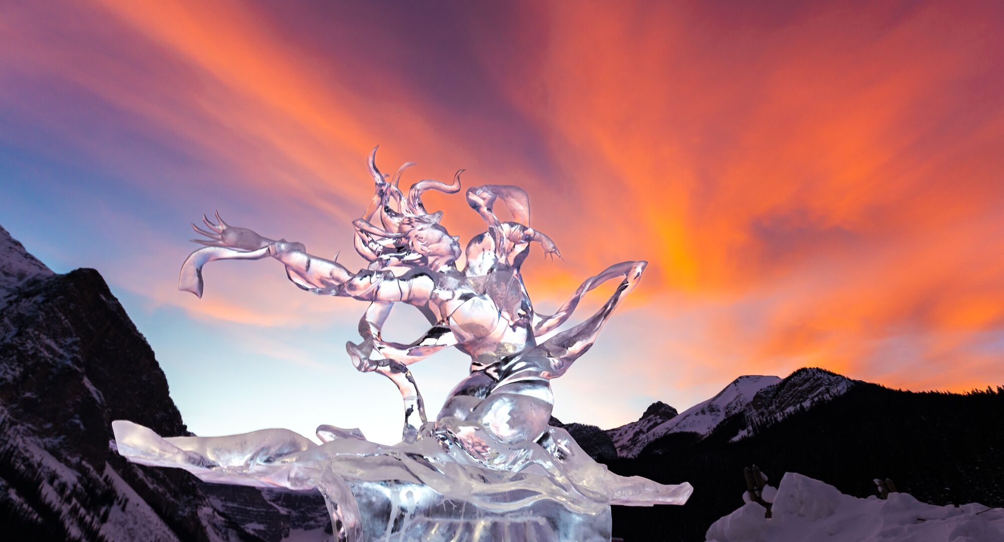 An ice sculpture of a woman dancing in front of a red sunset at Lake Louise.