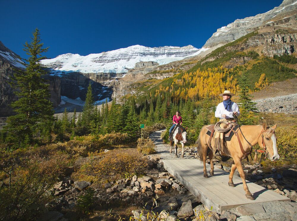 People on a guided horseback riding tour in Lake Louise with Victoria Glacier in the background