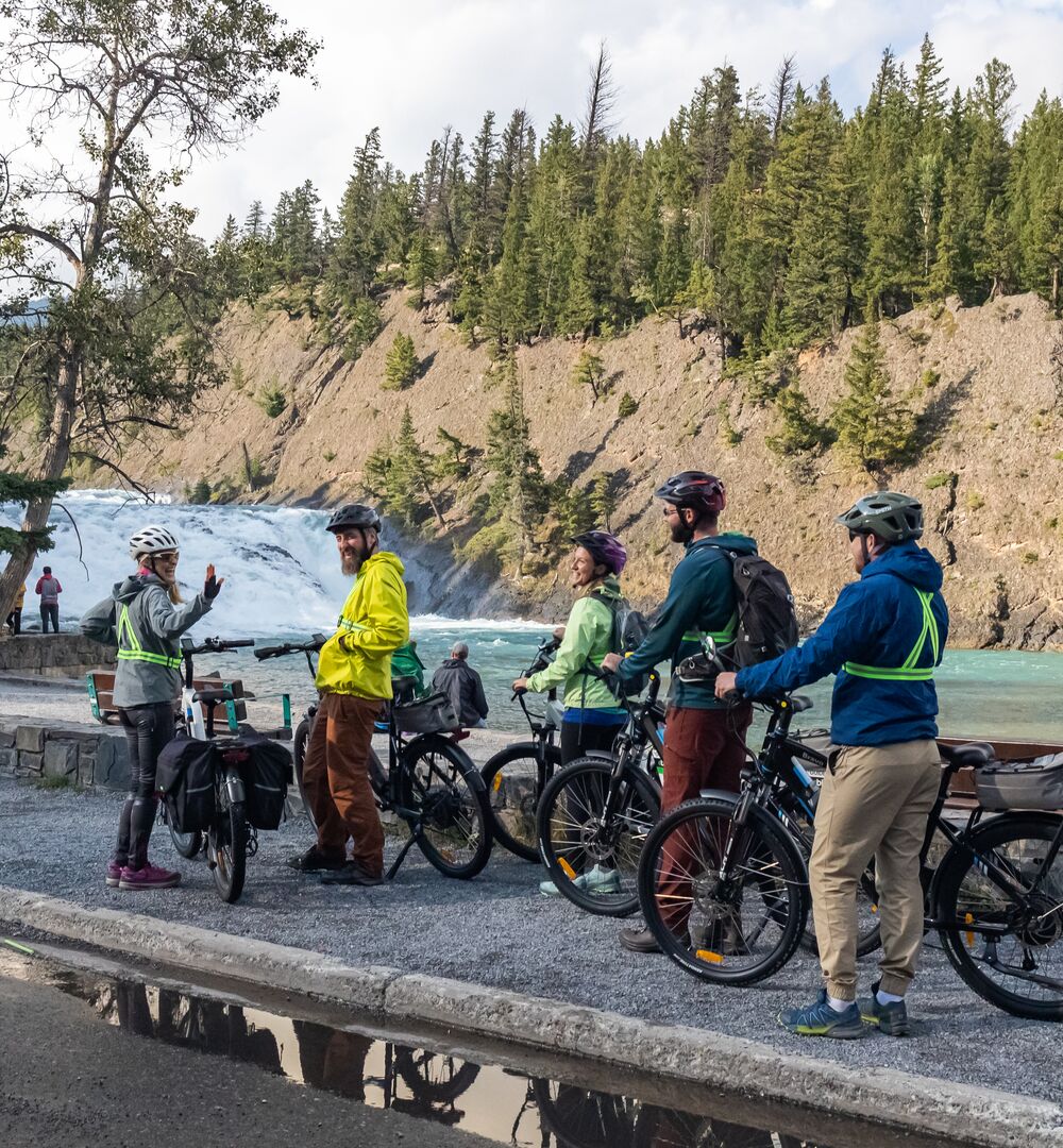 A group of people on a guided e-bike tour, standing in front of Bow Falls in Banff town