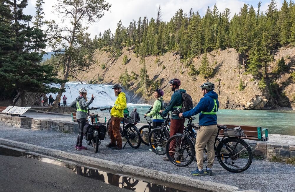 A group of people on a guided e-bike tour, standing in front of Bow Falls in Banff town
